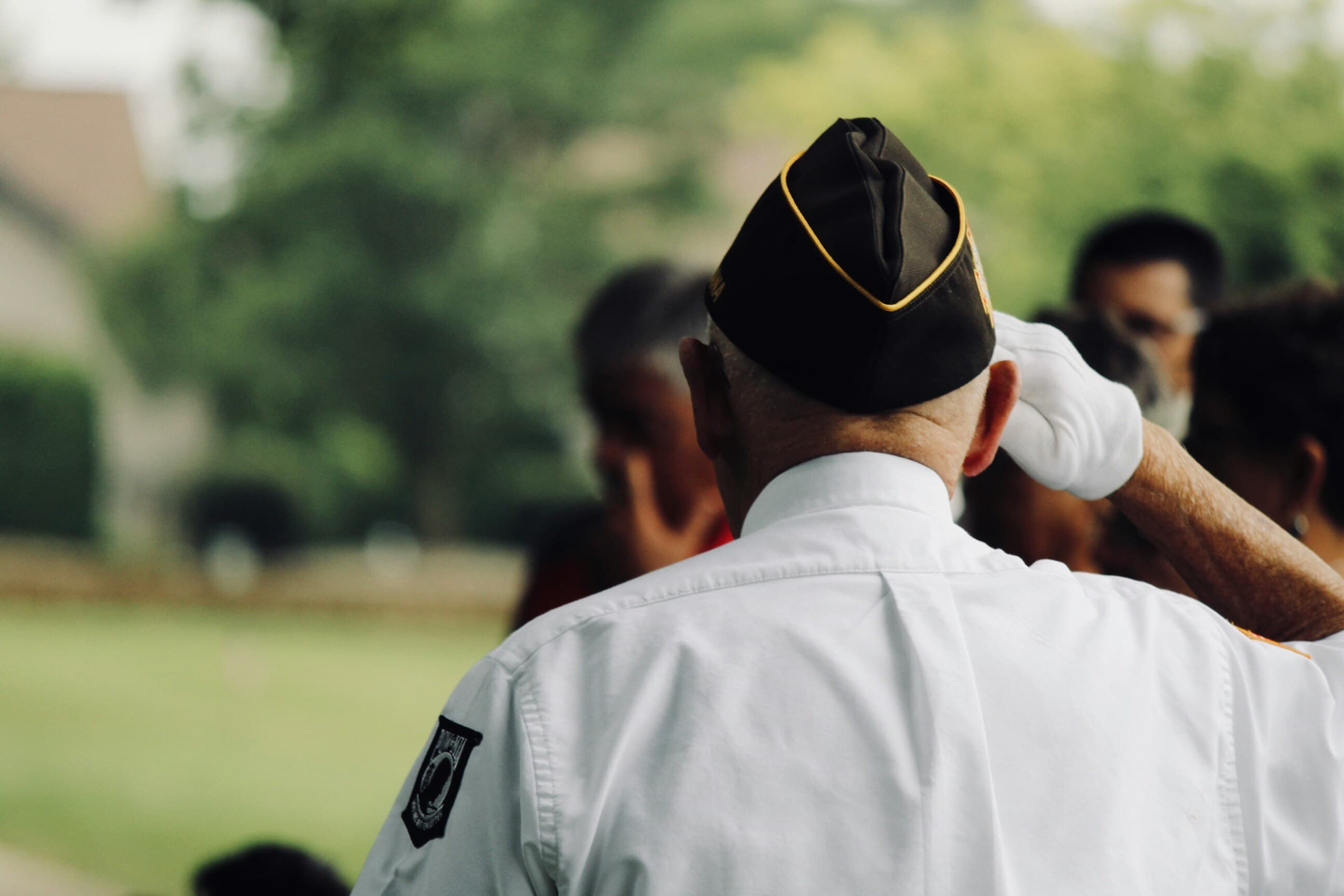 A veteran in dress uniform and white gloves saluting at an outdoor ceremony